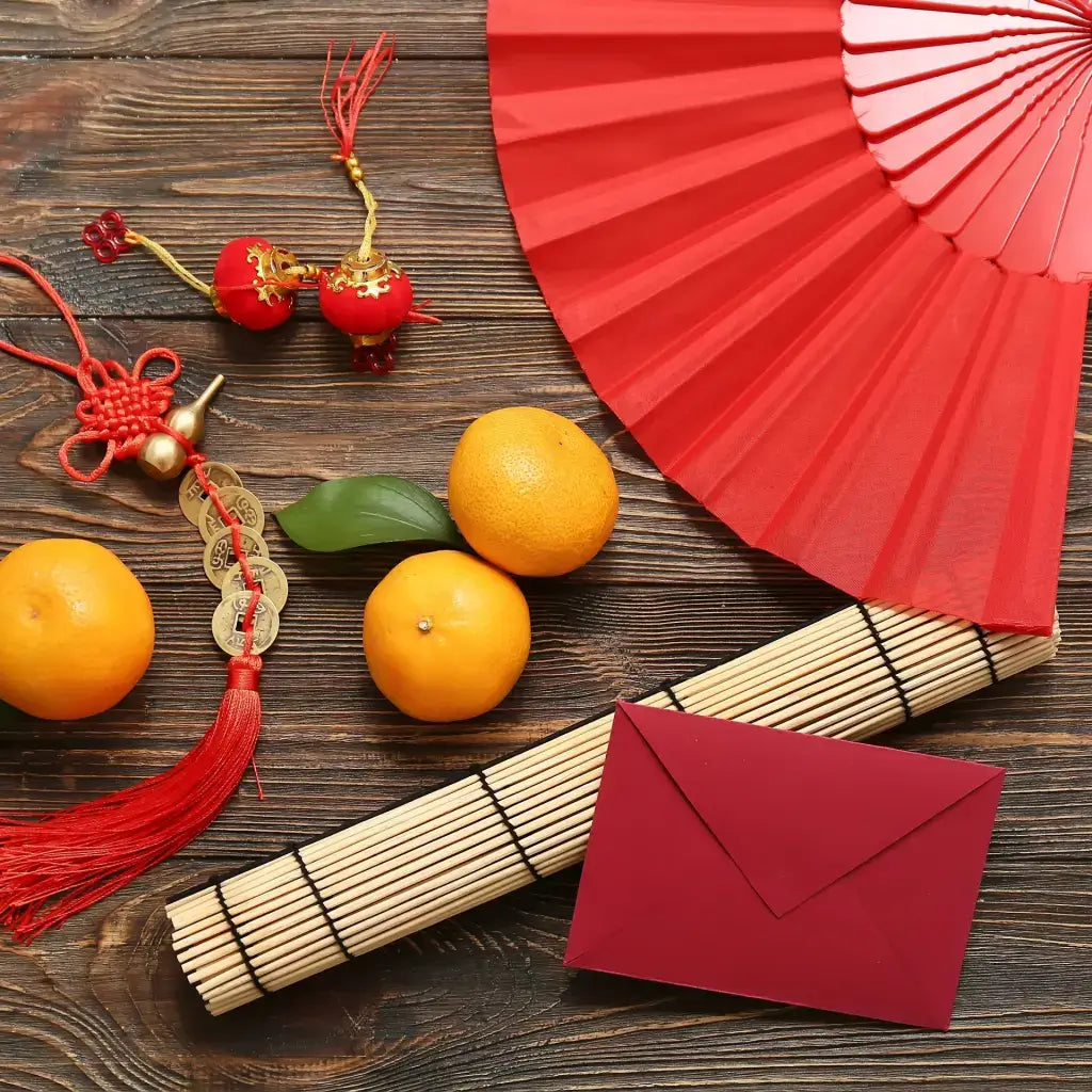 A bunch of Lunar New Year decorations. There's a red money envelope, fan and tassels next to mikan. 